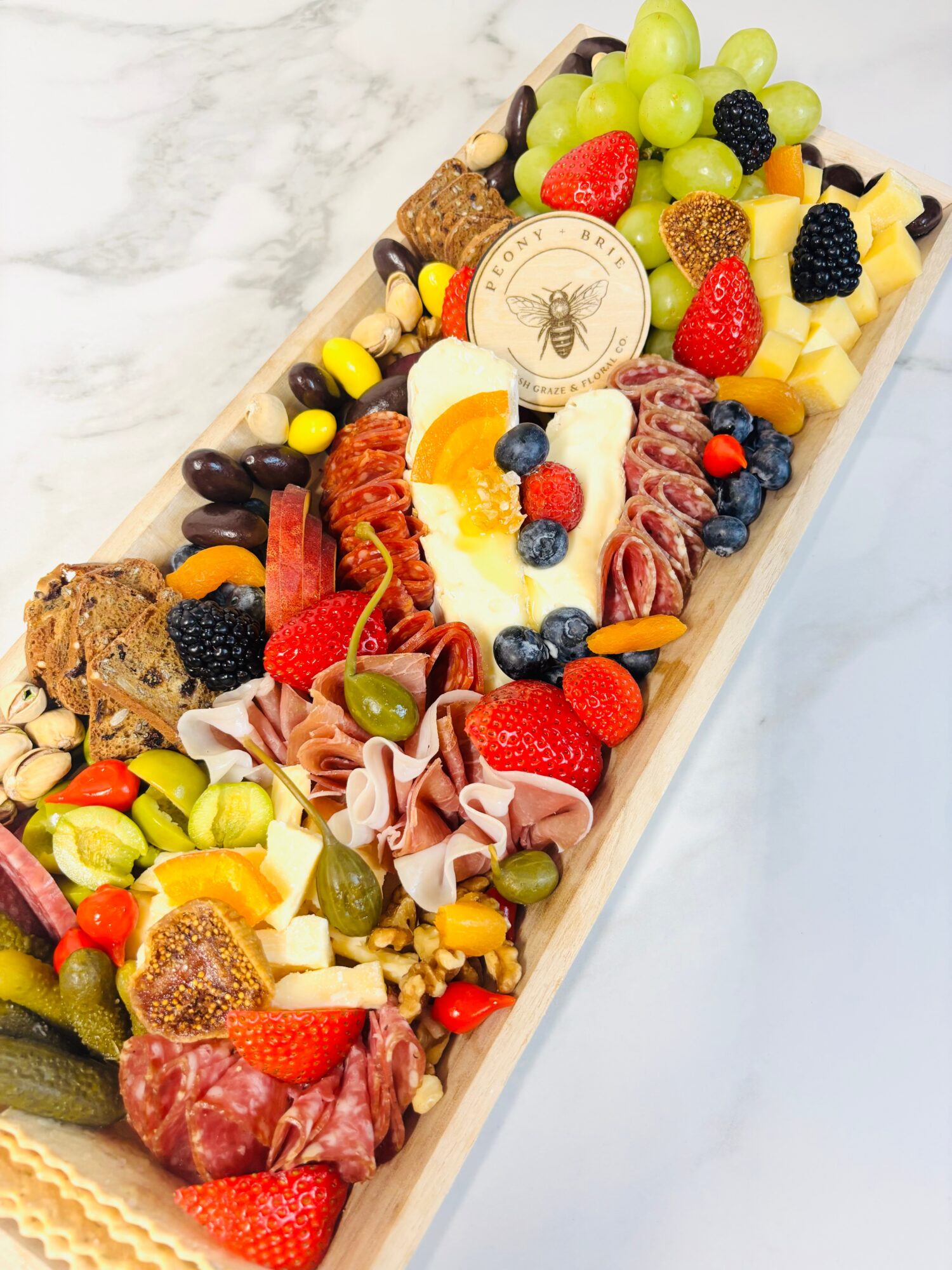 Long platter topped with grapes, berries, cheese, sliced meats, crackers, and a round decorated cookie.