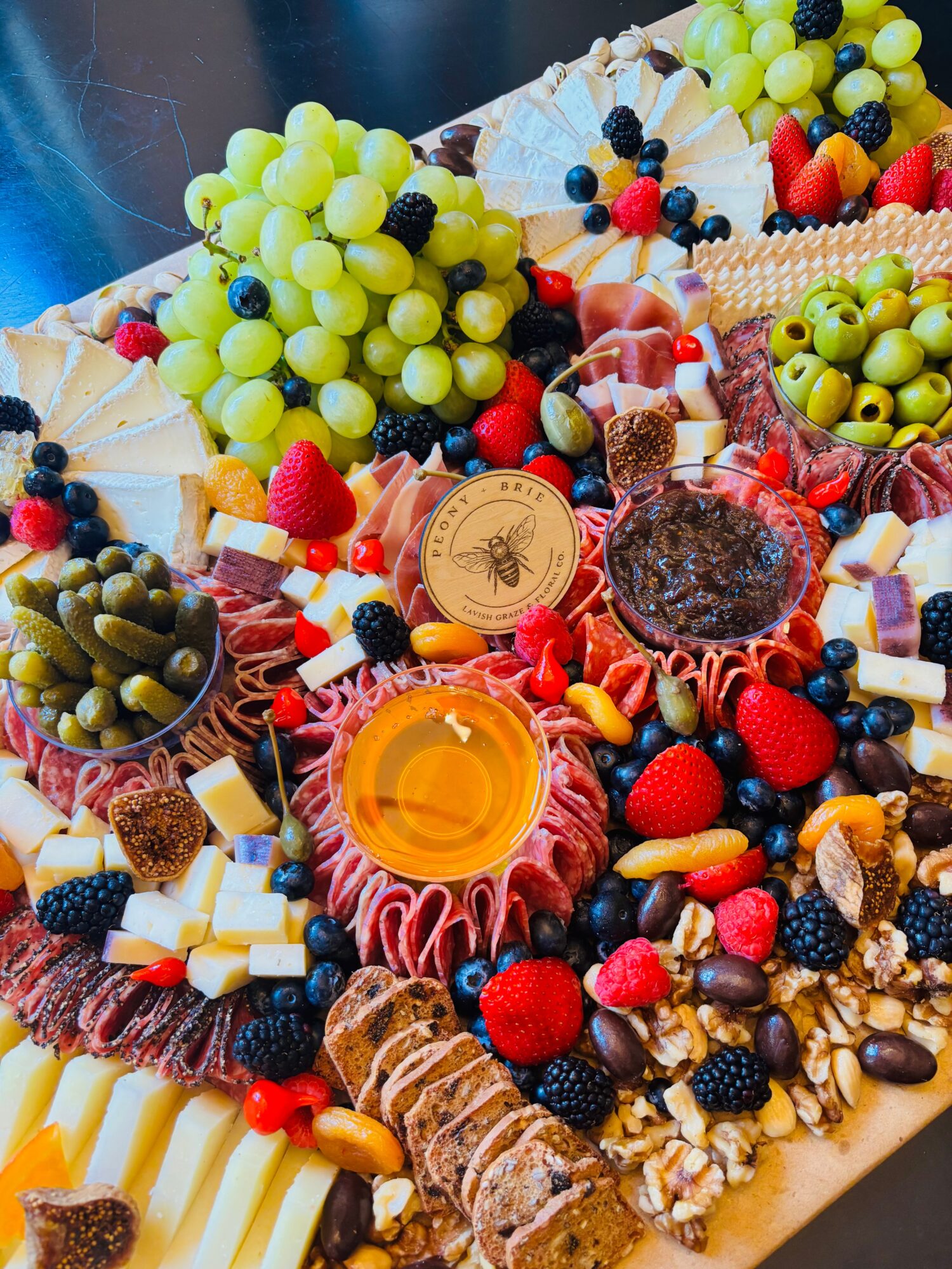 A table covered with grapes, berries, olives, cheeses, cured meats, pastries, and dips.