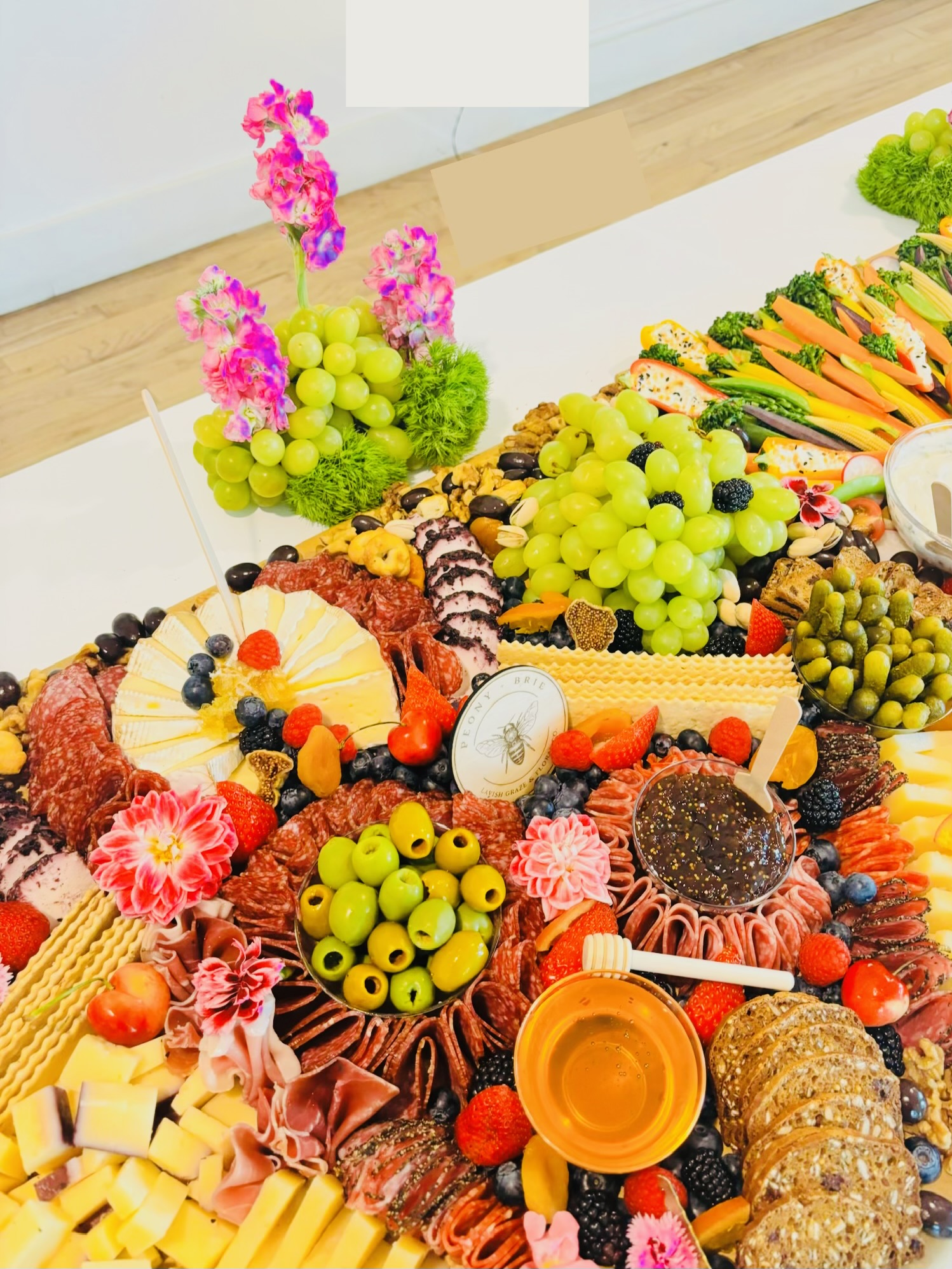 A colorful spread of fruit, vegetables, cheeses, meats, bread, and flowers arranged on a table.