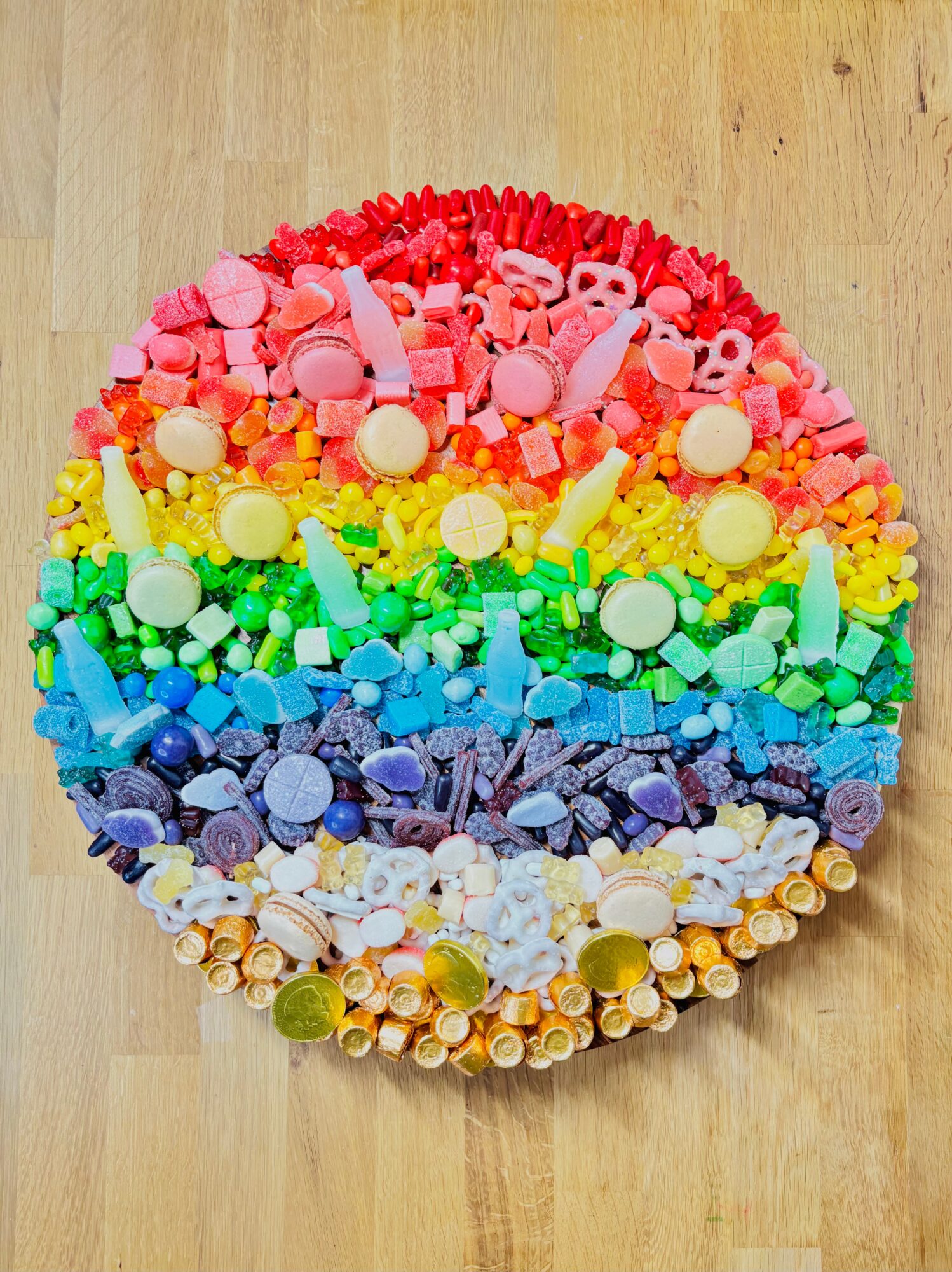Circular artwork made from small colorful objects arranged in rainbow bands on a wooden floor.