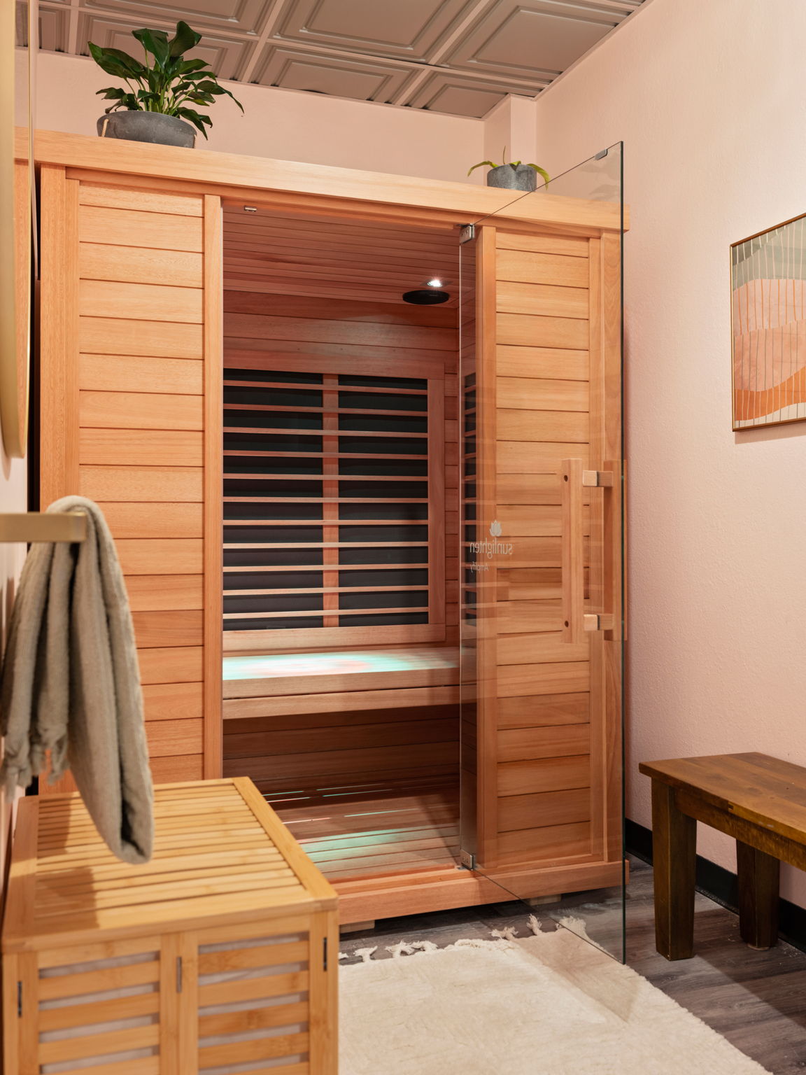 Wooden sauna with glass door, slatted benches, a hanging towel, and a small table.