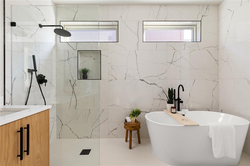 Modern bathroom with a freestanding bathtub, wood vanity, glass shower partition, and marble-patterned walls.