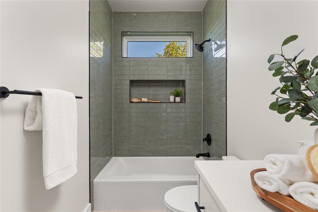 Modern bathroom with a tiled shower, bathtub, towel rack, vanity, and leafy plant.