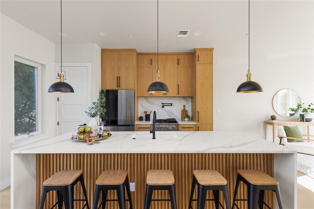 Bright kitchen with wooden cabinets, a marble island, four stools, and pendant lights.