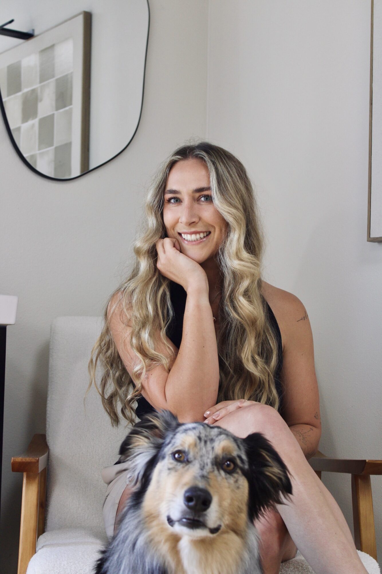 A seated person with long wavy hair rests a hand on a dog sitting on their lap.