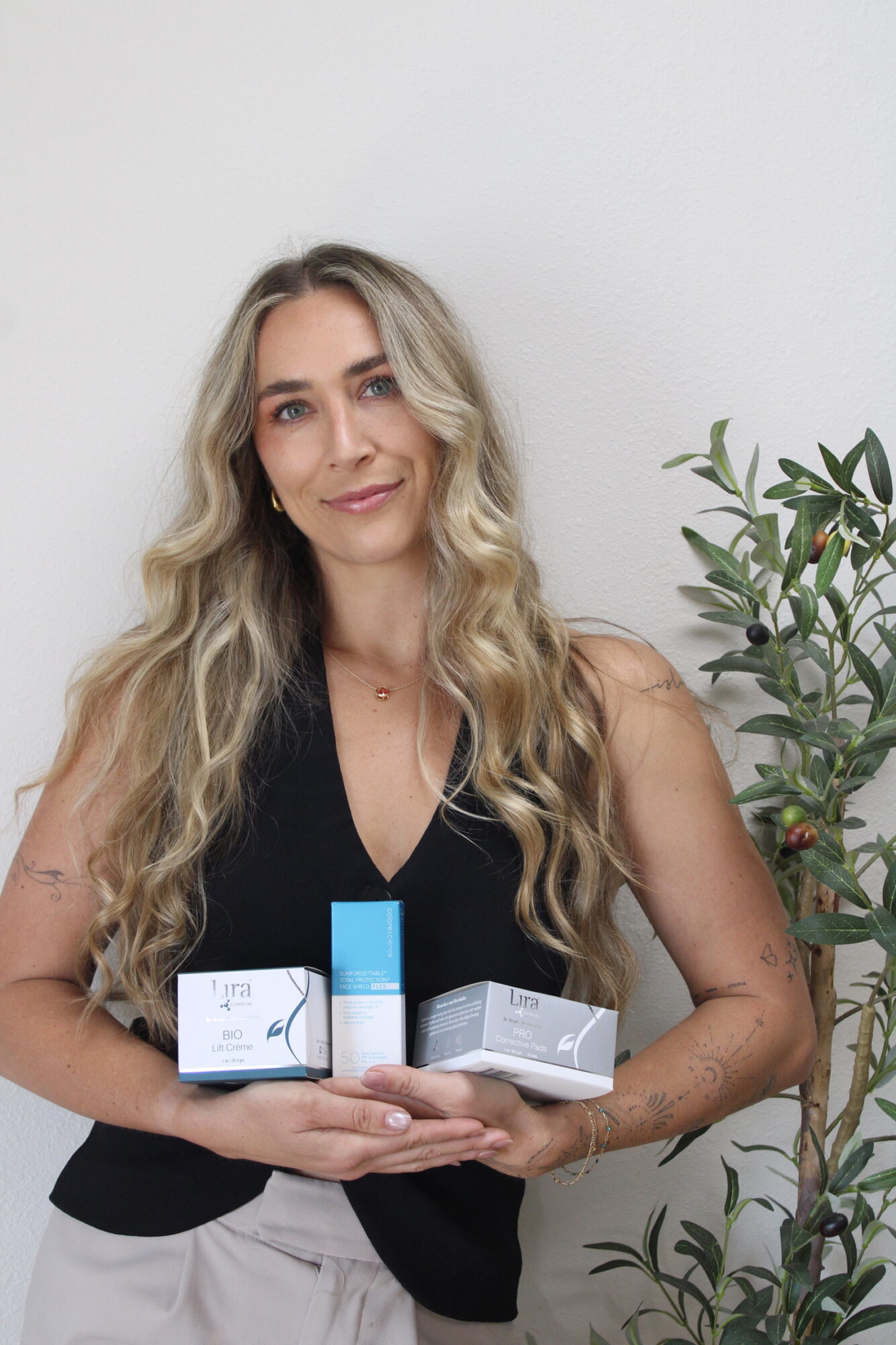 Person holding two product boxes while standing beside a leafy plant.