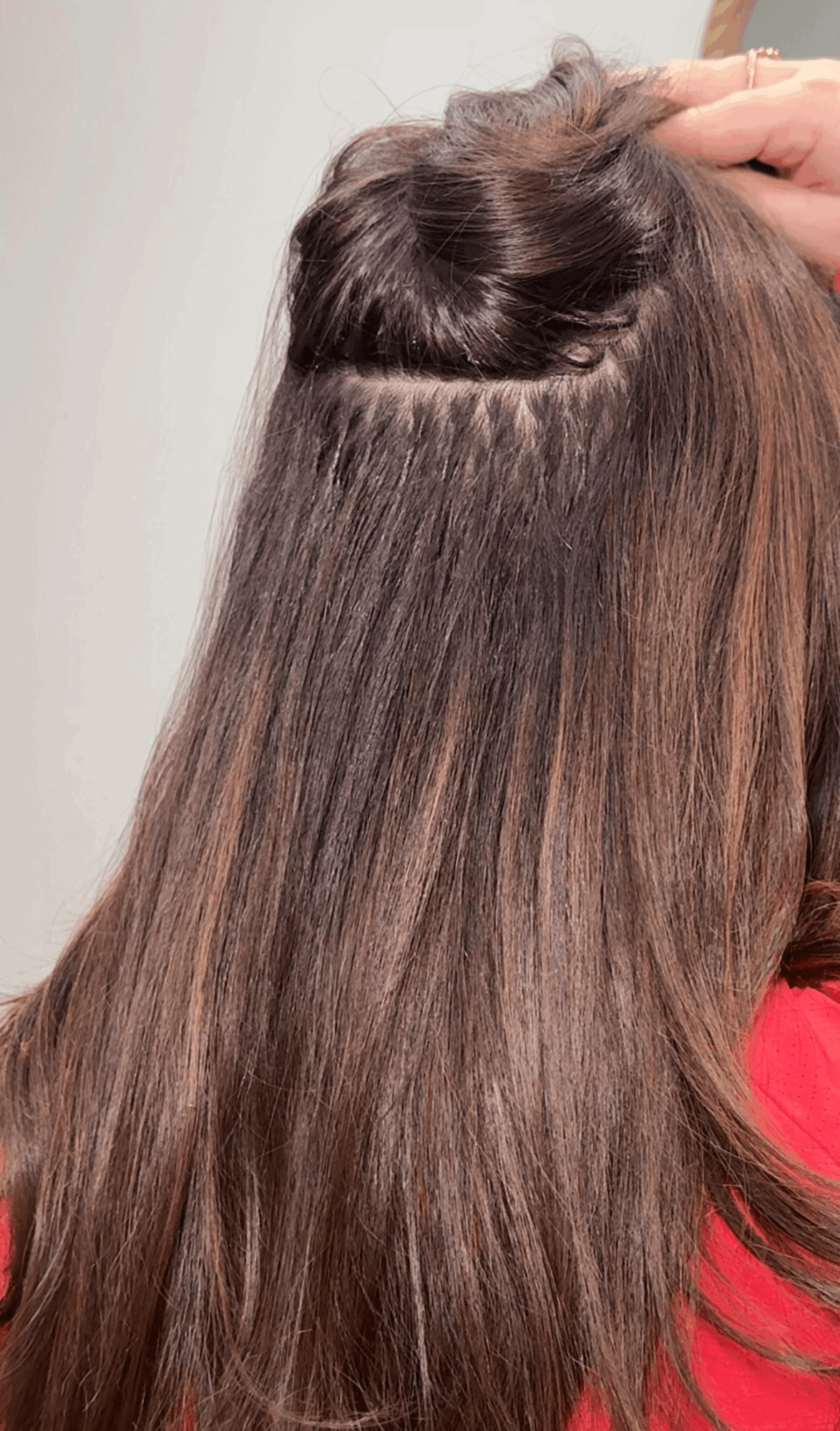 Long brown hair is parted horizontally, with a hand lifting a section near the crown.