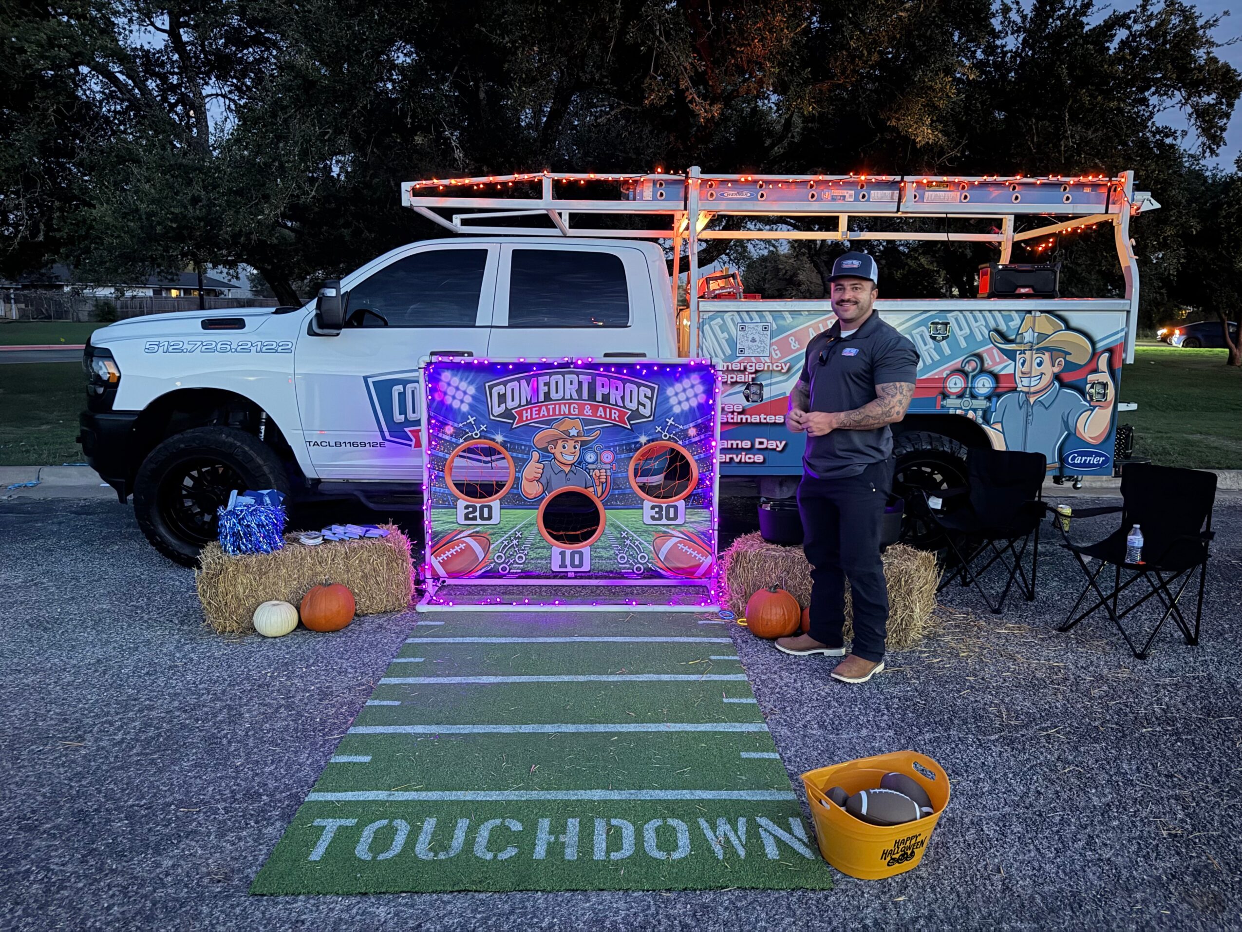 A person stands beside a decorated truck and colorful display at an outdoor event, with a football field mat in front.