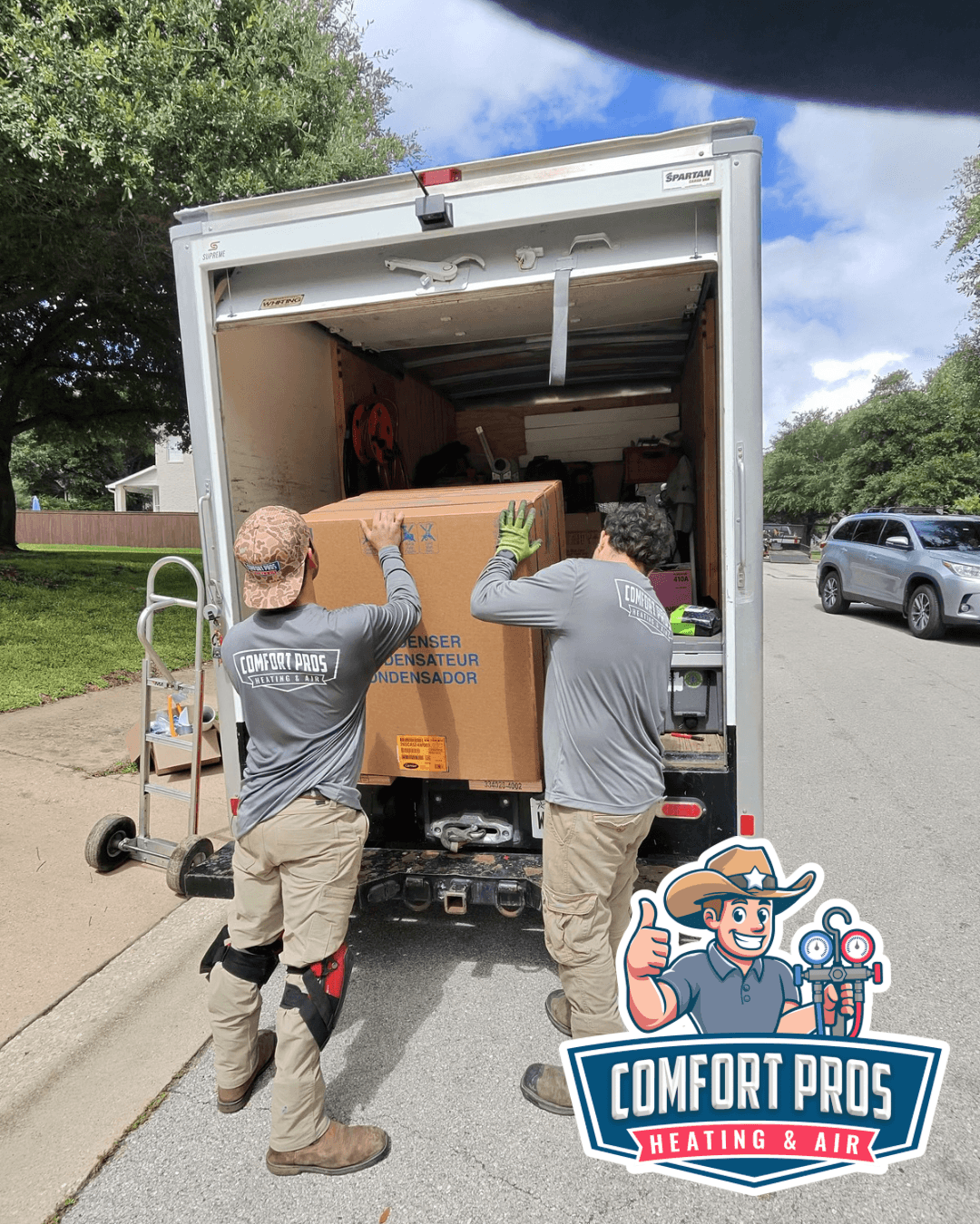 Two workers load a large box into the back of a moving truck parked on a street.