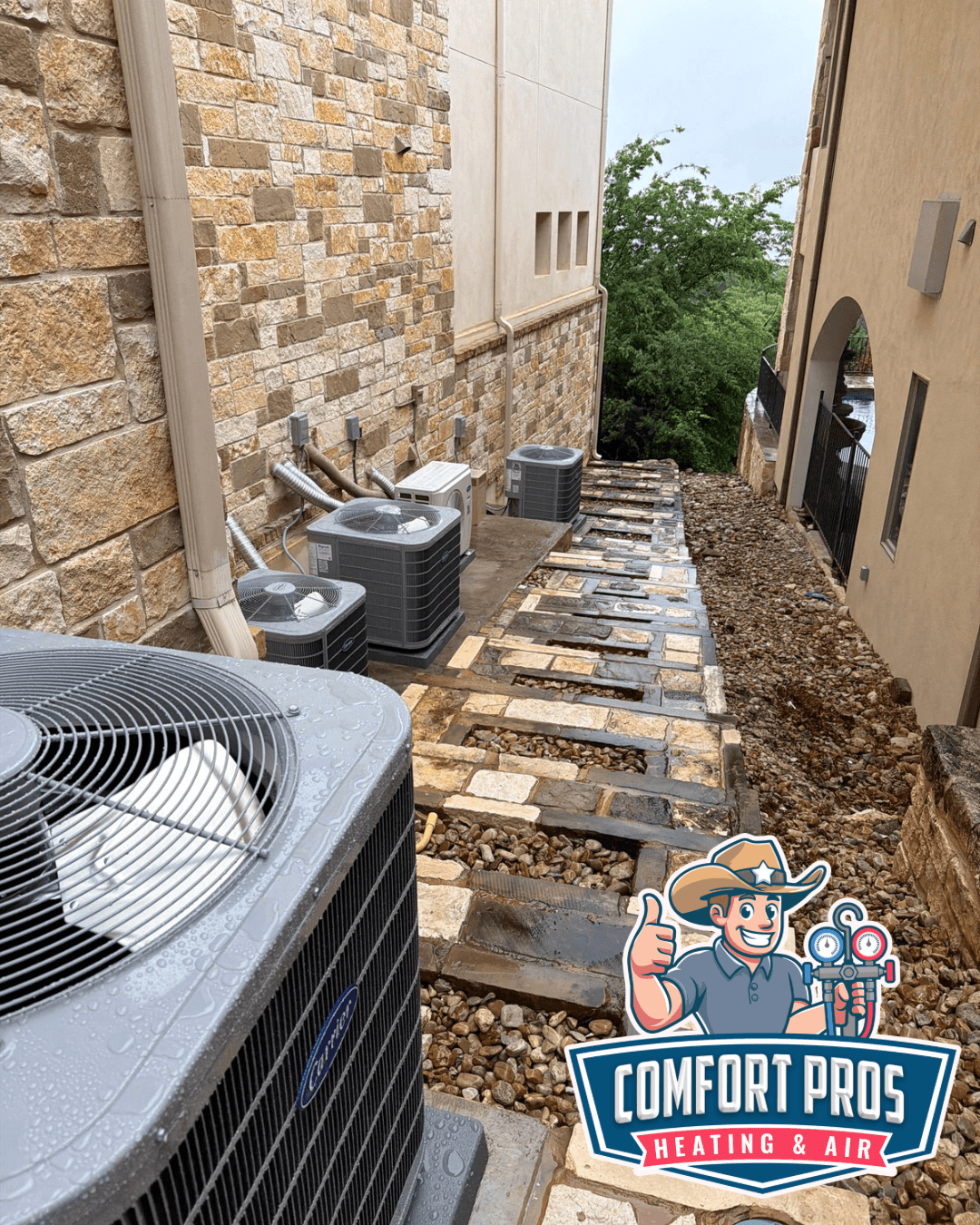 Air-conditioning units beside a narrow stone-paved passage between buildings, with a Comfort Pros logo at the bottom.