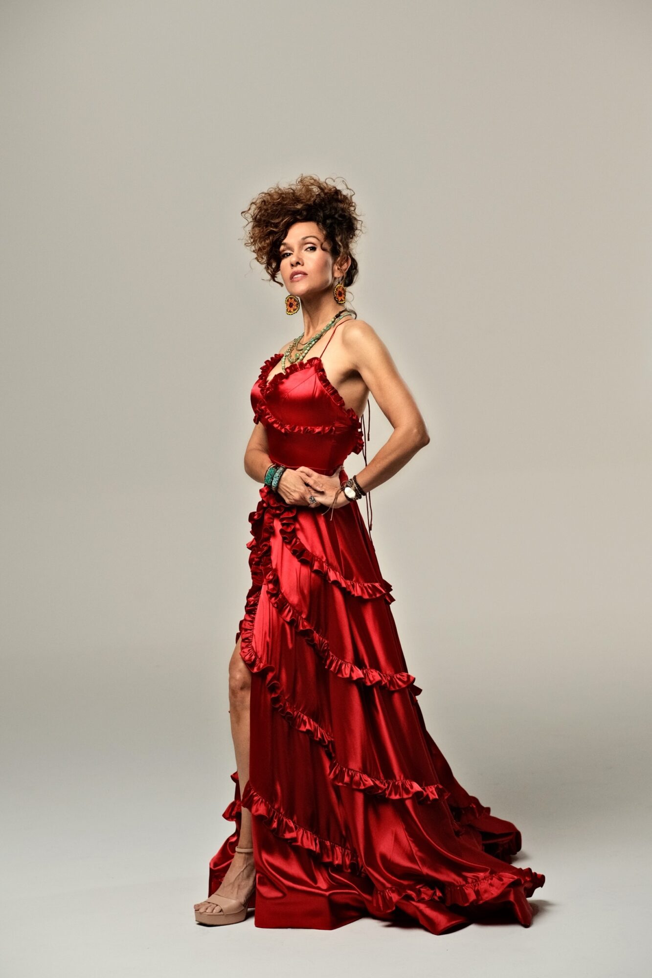 A person poses in a long red ruffled dress against a plain light background.