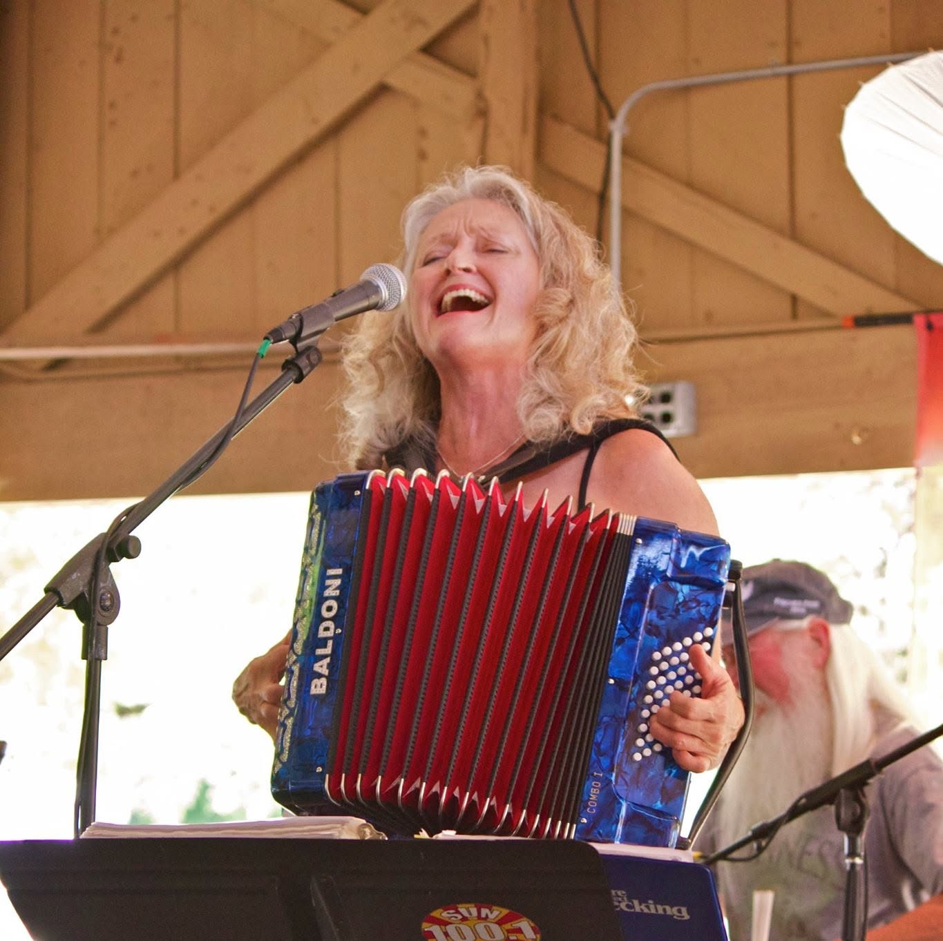 A person sings into a microphone while playing a red and blue accordion.