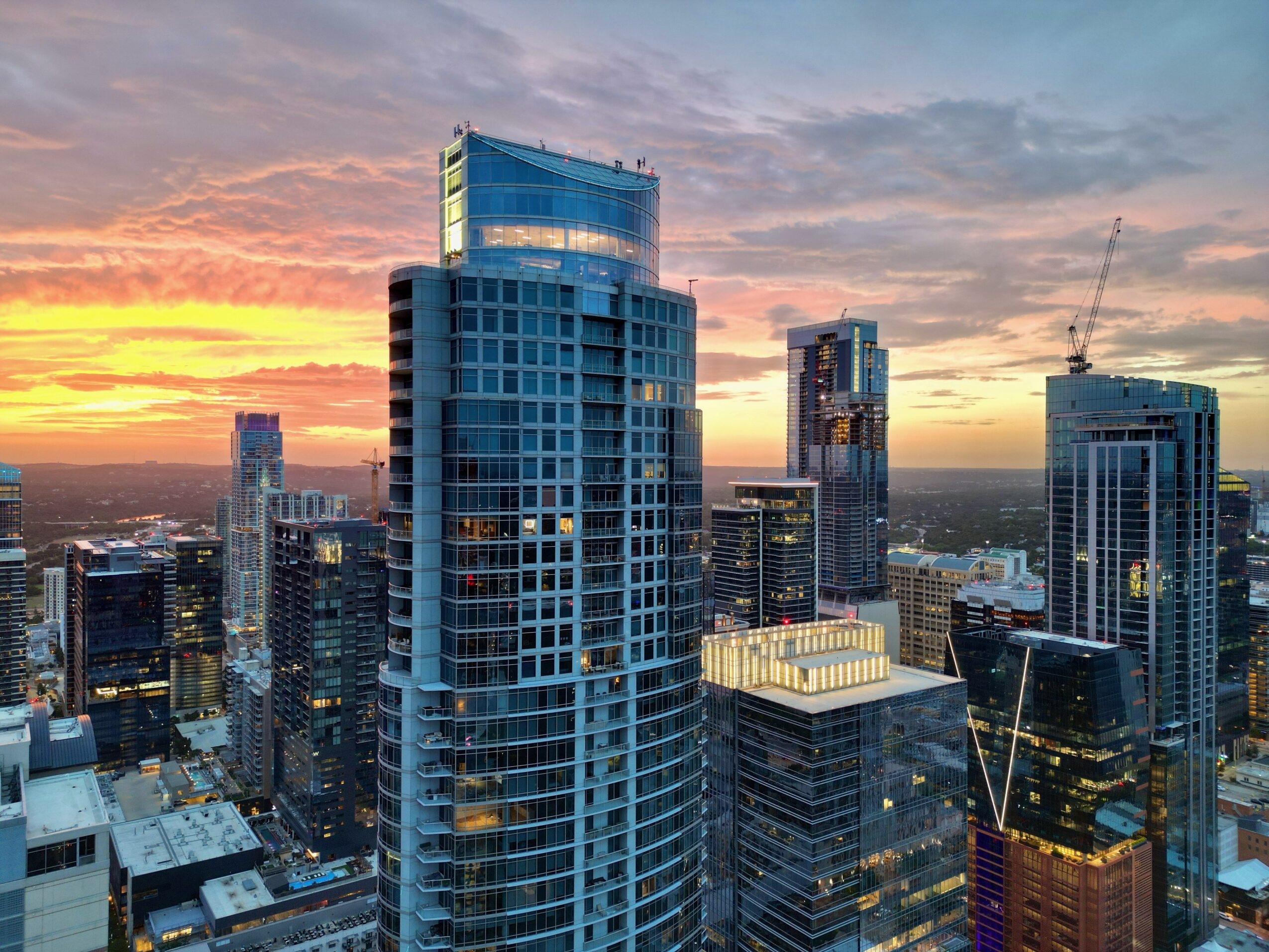 City skyline with tall glass skyscrapers beneath a colorful sunset sky.