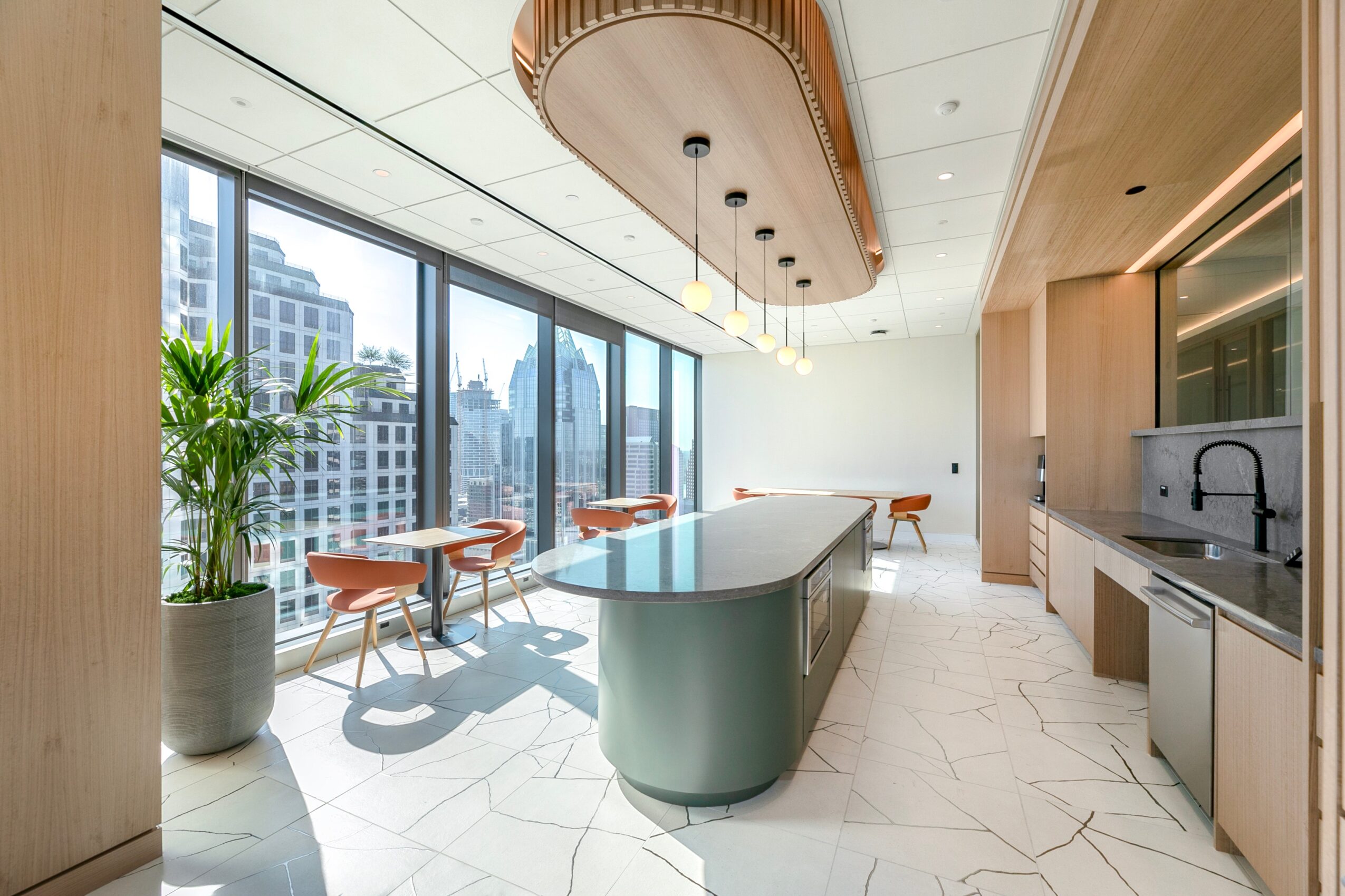 Bright modern kitchen with a central island, pendant lights, dining stools, and large windows overlooking city buildings.