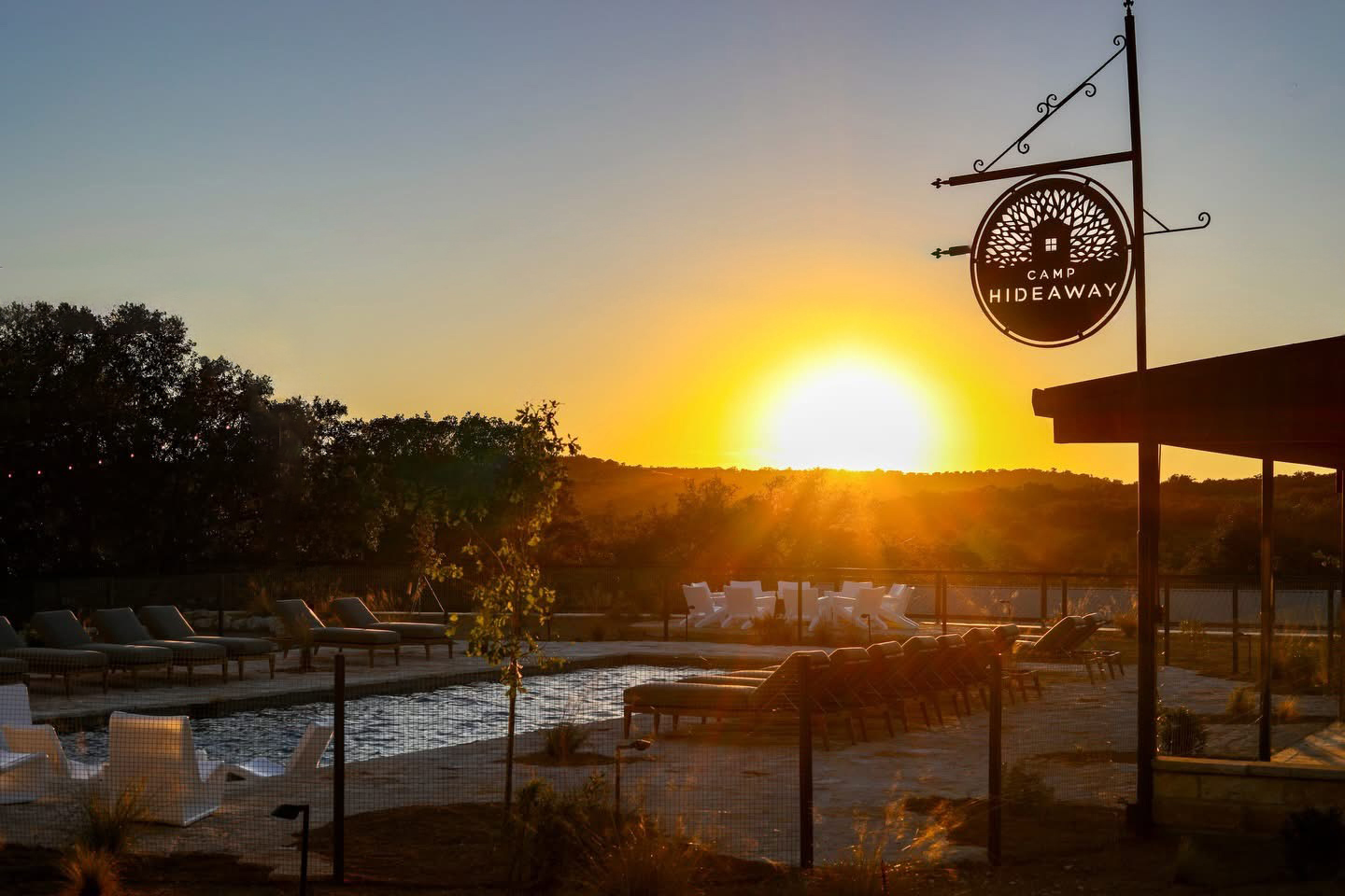 Sunset over an outdoor pool with lounge chairs and a hanging sign reading “Hideaway.”