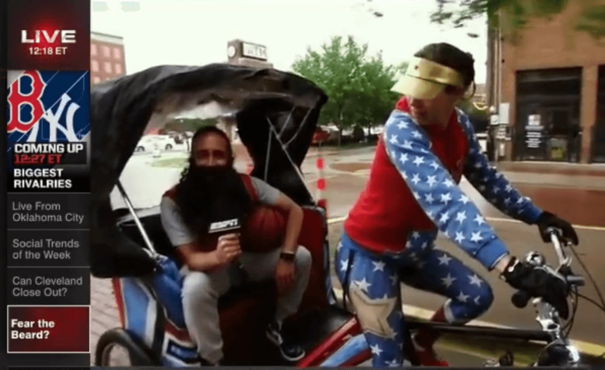 A person sits in a covered pedicab while another person wearing a star-patterned outfit rides a bicycle beside them.