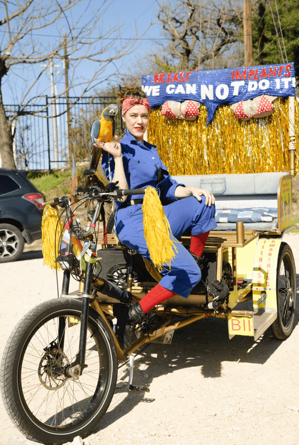 Person seated on a decorated three-wheeled bicycle in front of a blue and gold display.