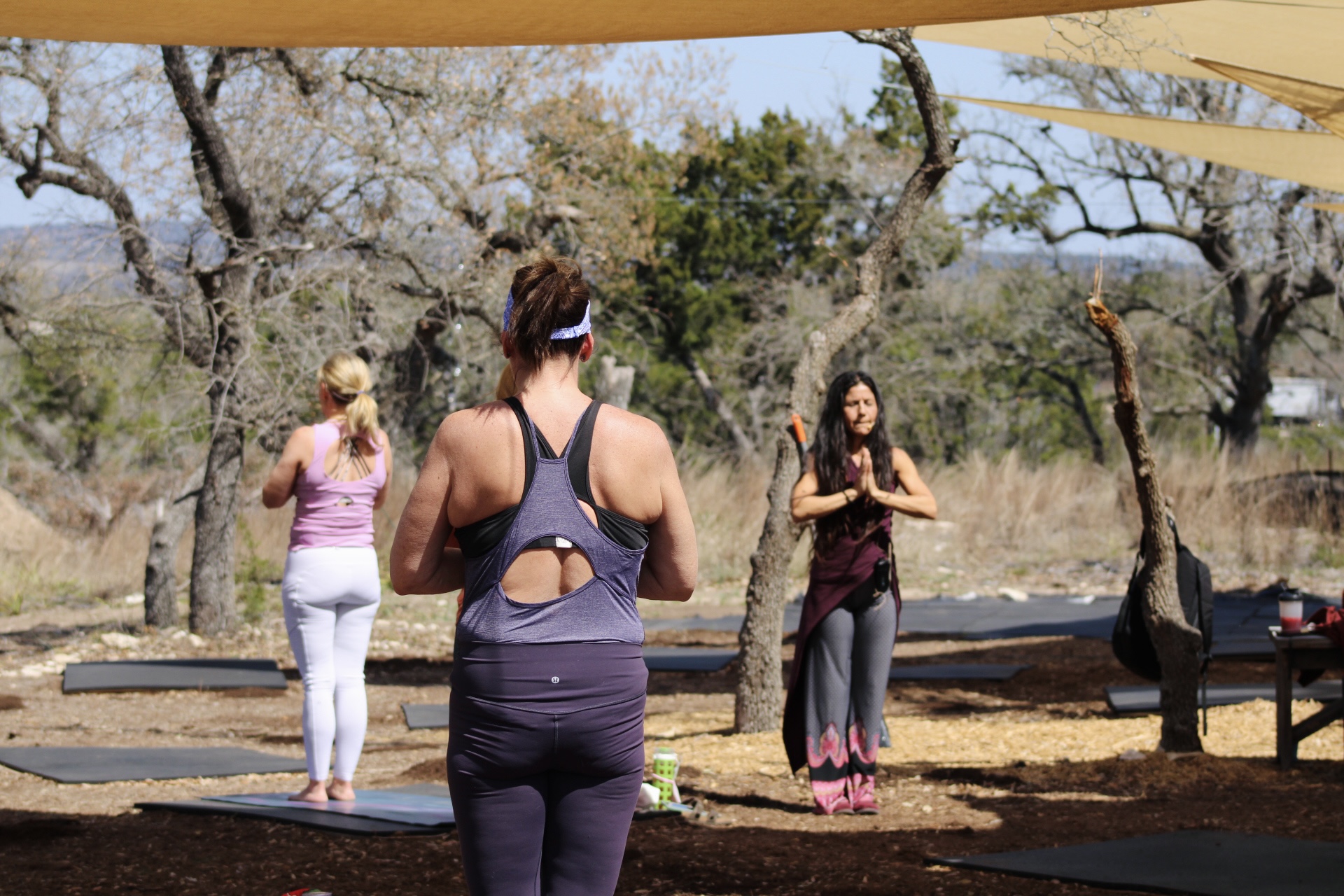Two people exercise beneath a canopy in a wooded outdoor area, with another person standing nearby.
