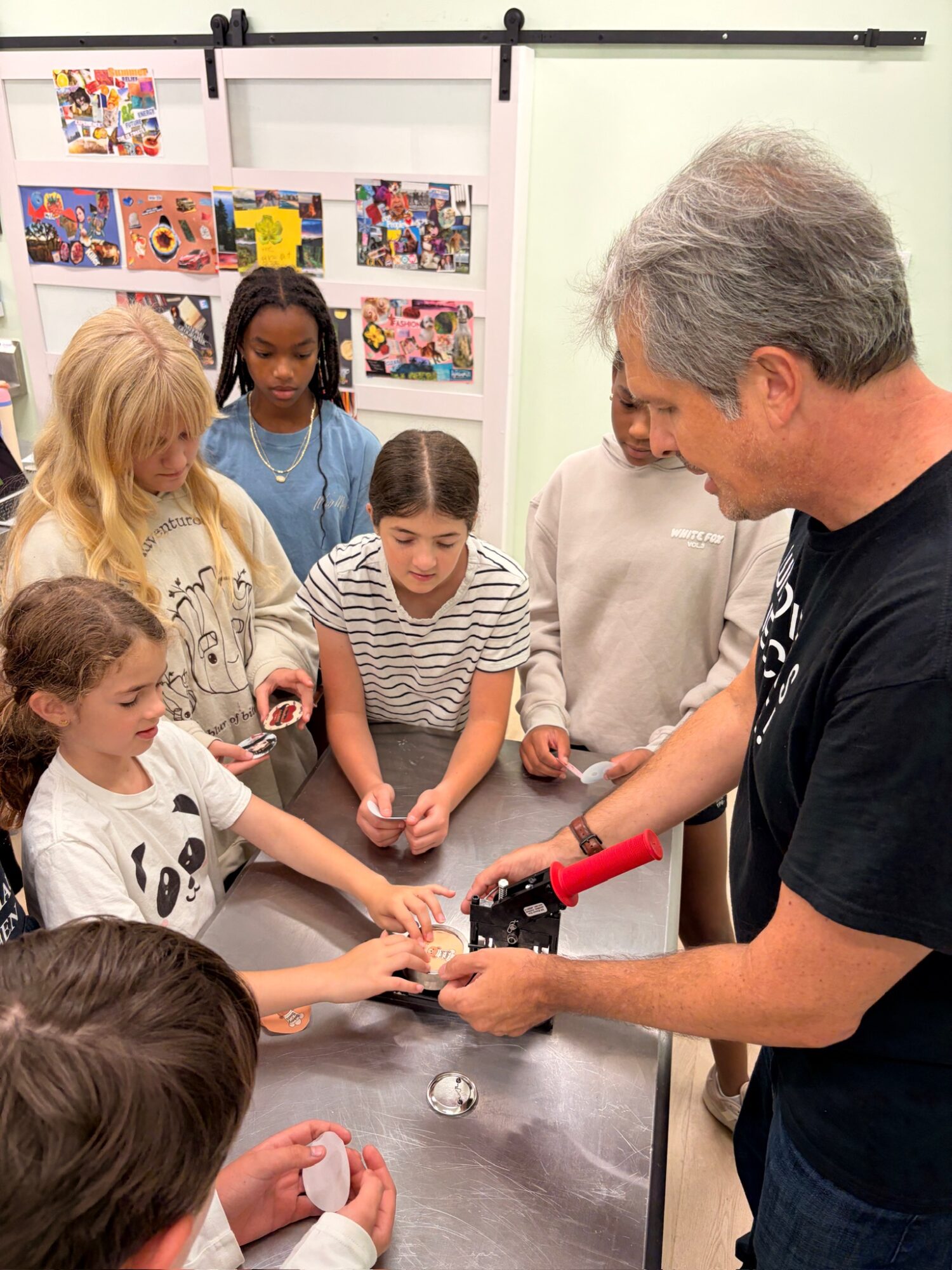 A man demonstrates a red-handled tool to several children gathered around a table.