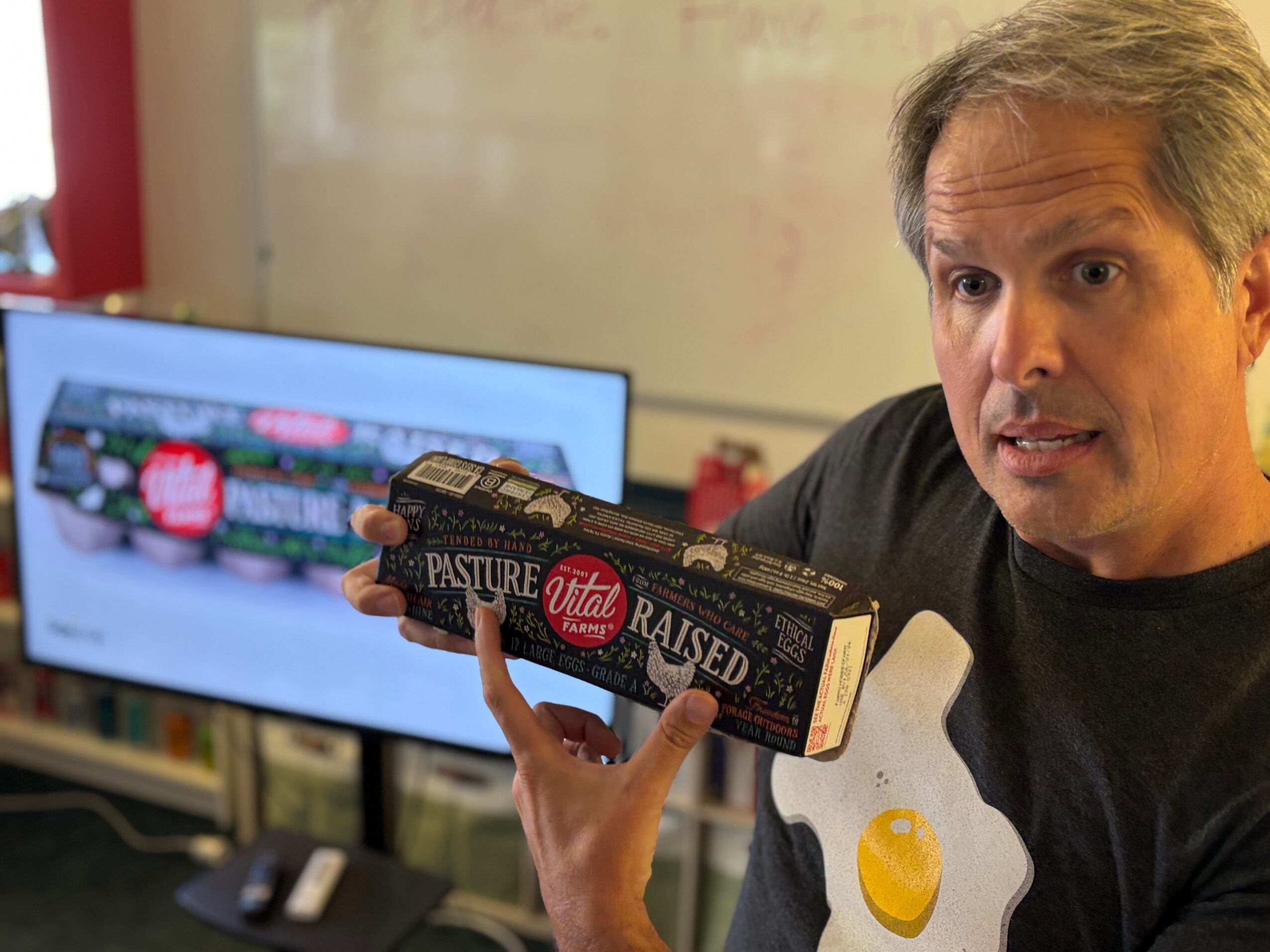 A person holds a chocolate bar beside a computer monitor displaying food images.