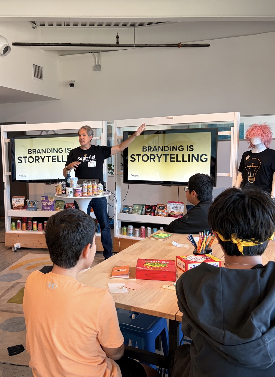 A presenter stands beside a screen reading “Branding is storytelling” as people sit around a table.