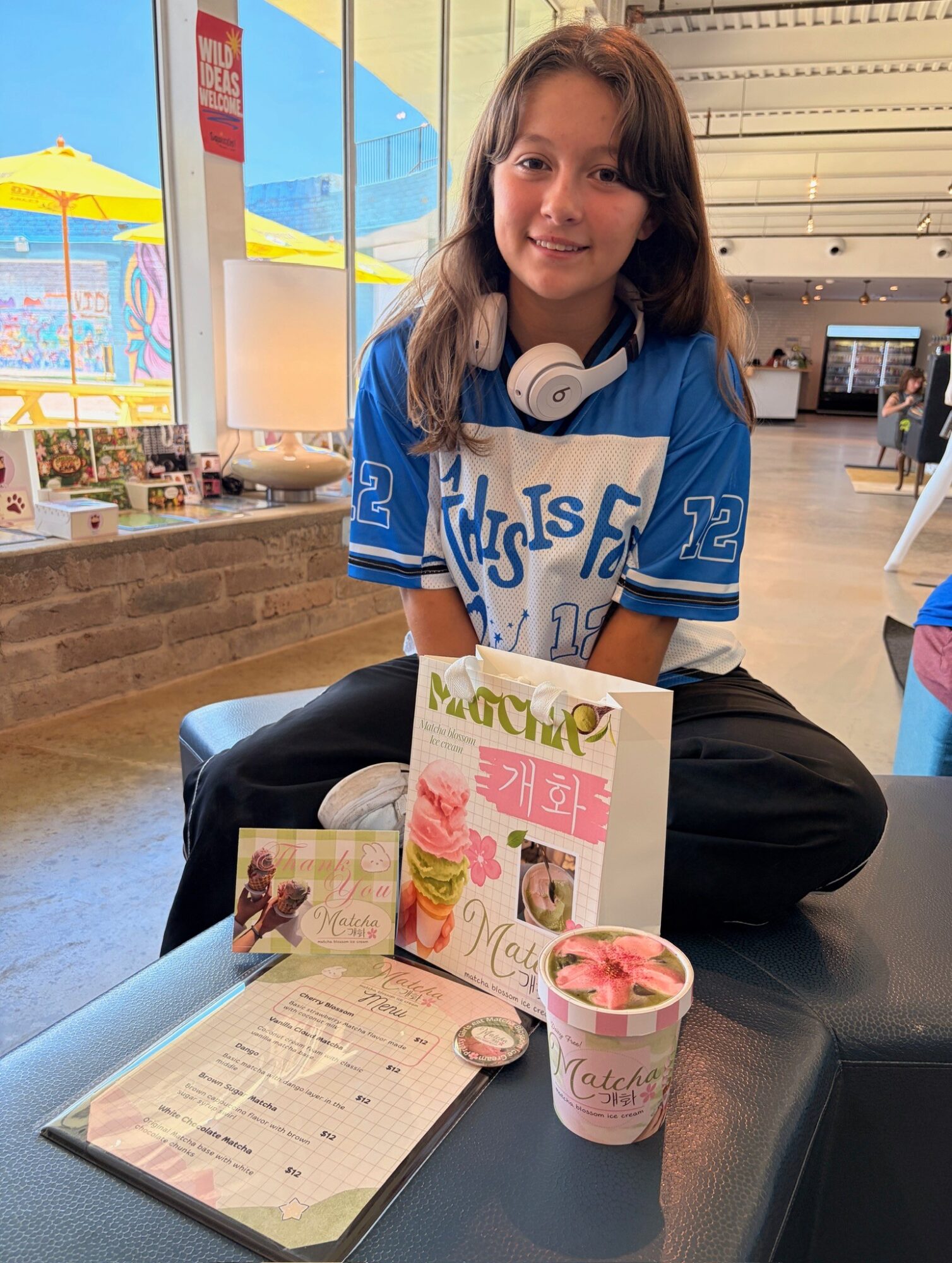 A person wearing a blue jersey sits at a table with a menu, dessert, and drink.