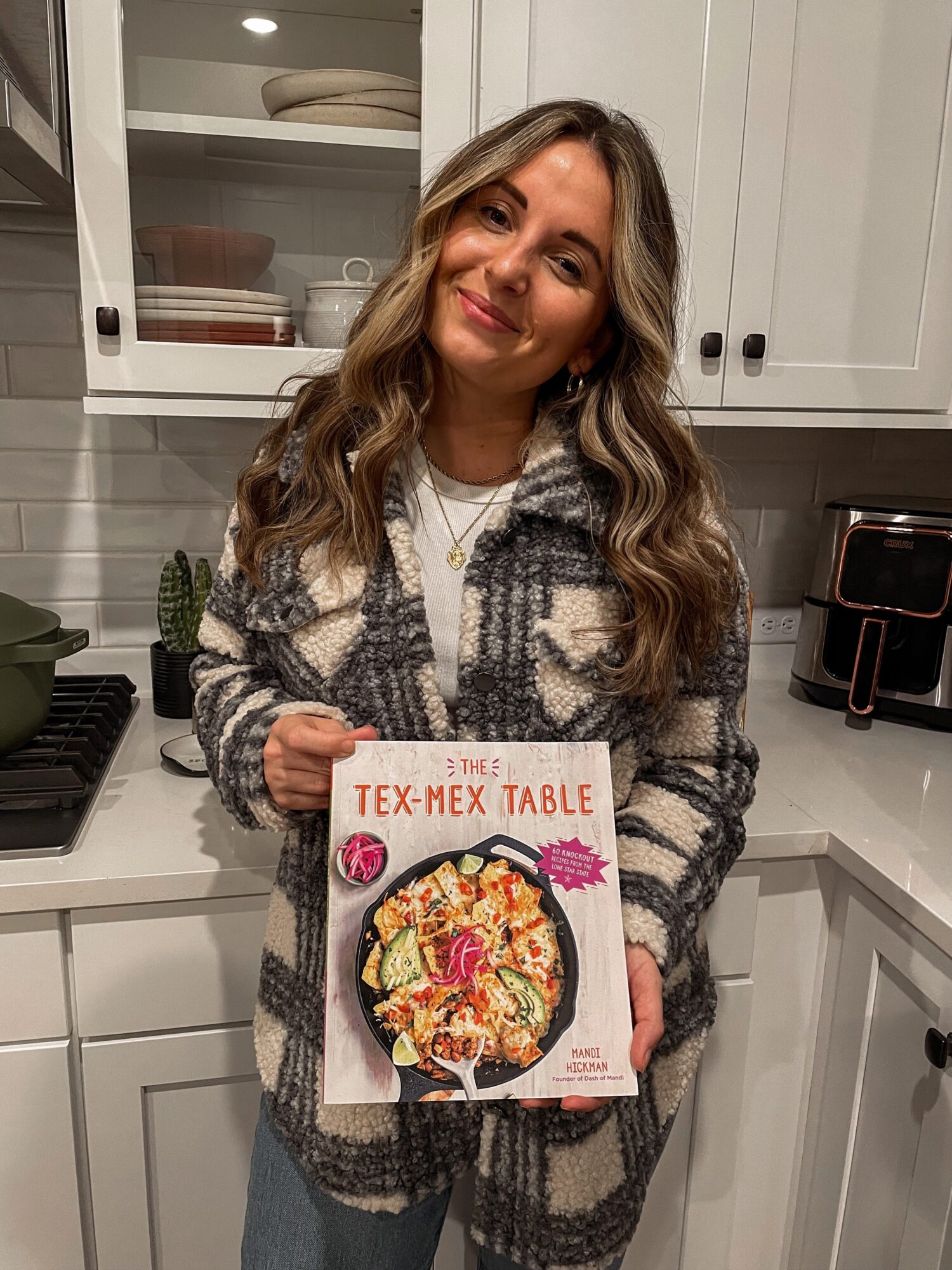 Person holding a cookbook titled “Tex-Mex Table” in a kitchen.