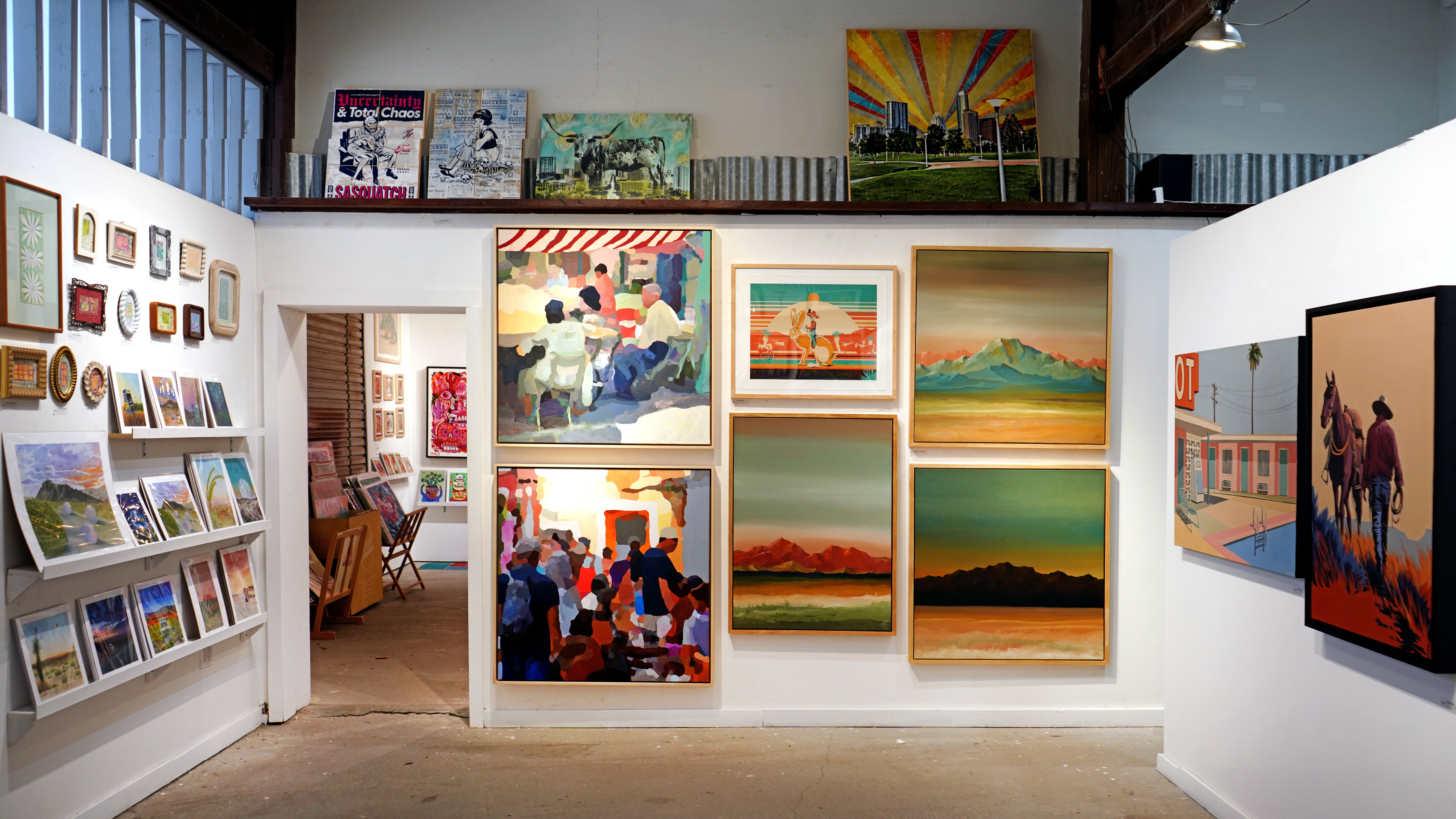 Art gallery interior with framed paintings displayed on white walls and shelves.