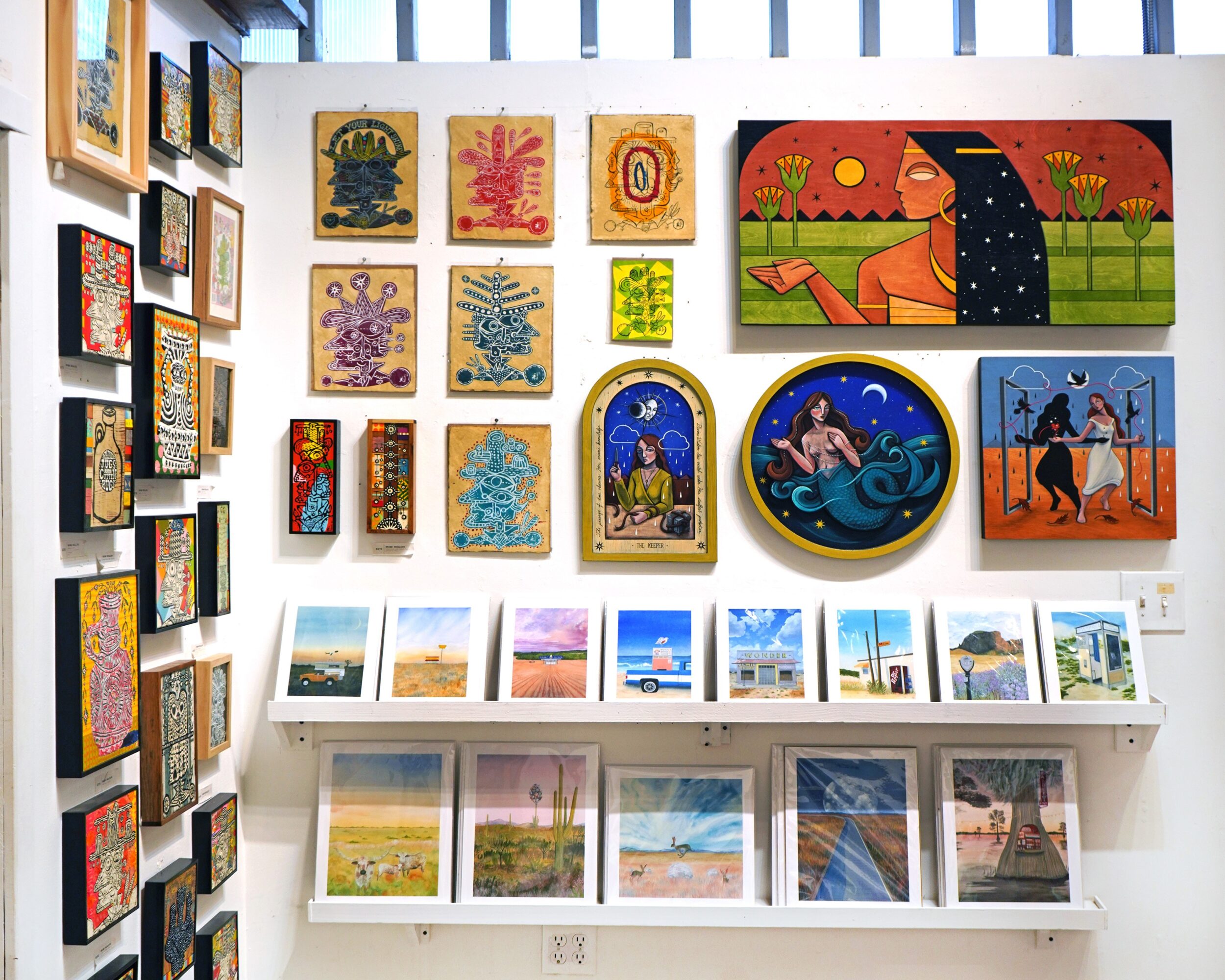 Gallery wall displaying colorful framed artwork above shelves of landscape prints.
