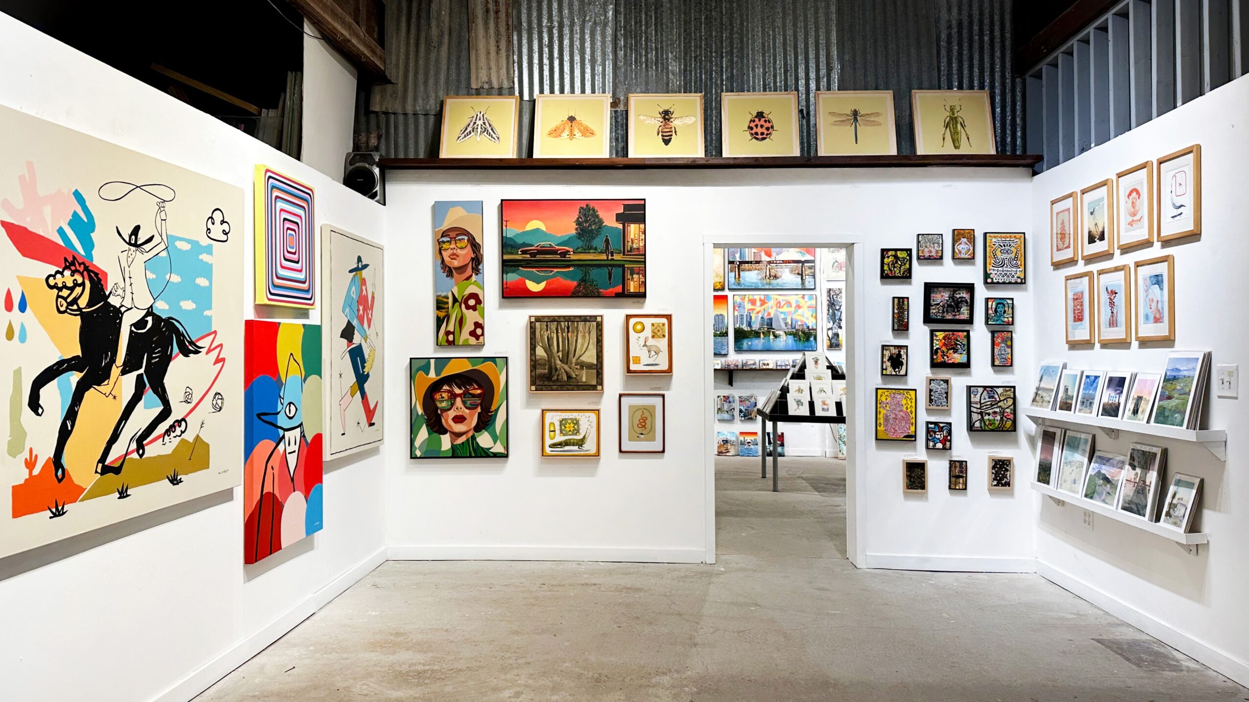 Art gallery with colorful paintings and framed artwork displayed on white walls.