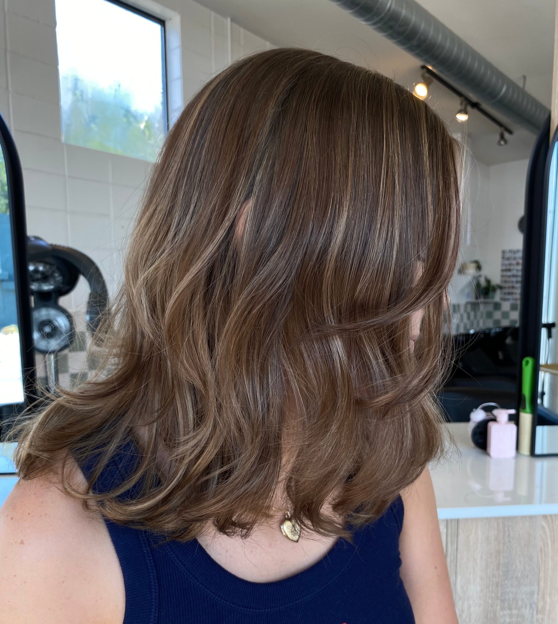 Back view of a person with shoulder-length wavy brown hair in a salon.