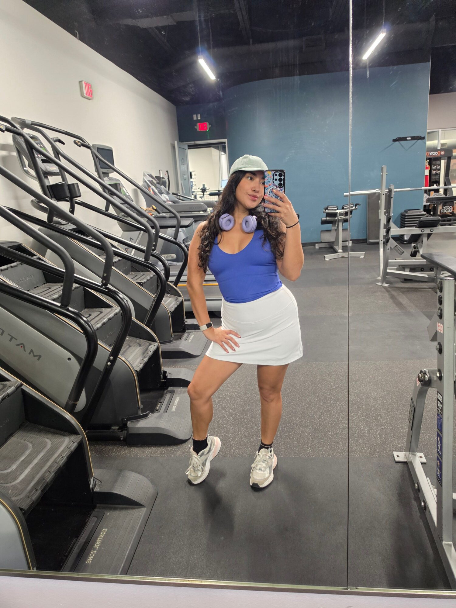 Person in a blue shirt and white shorts stands beside gym exercise equipment.