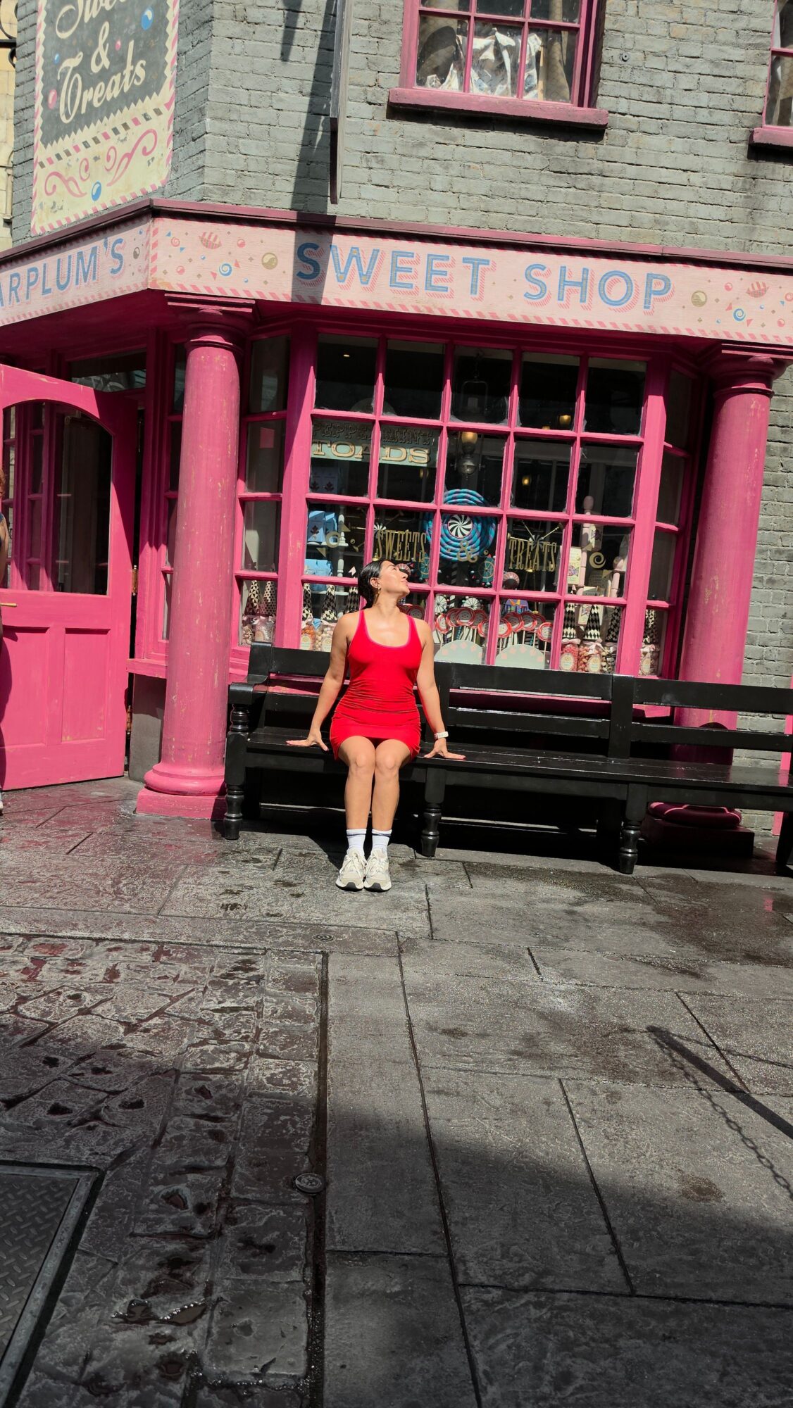 Person in a red outfit standing outside a pink shop with a large window.