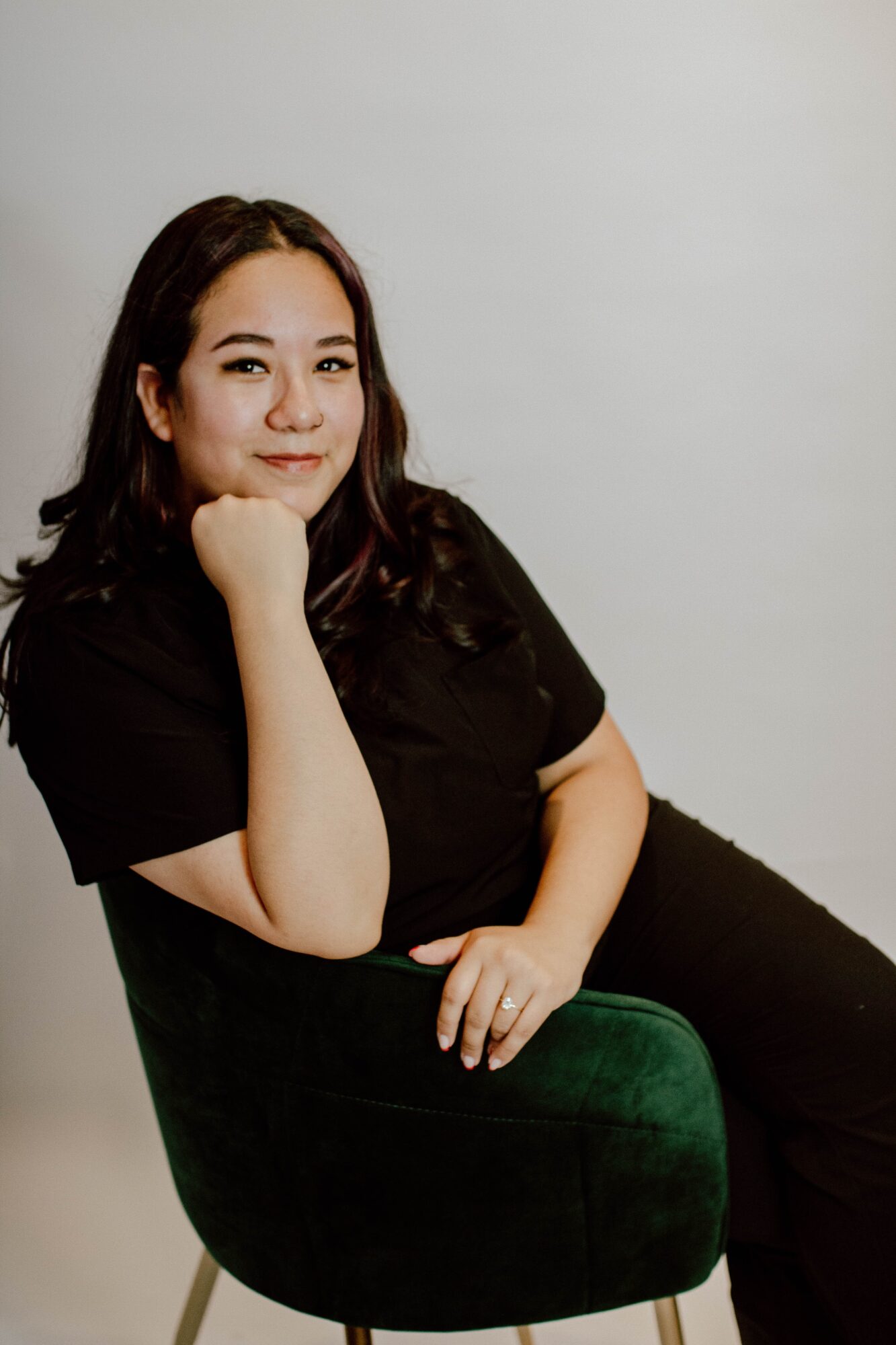 A seated person in a black shirt and green pants poses against a plain light background.