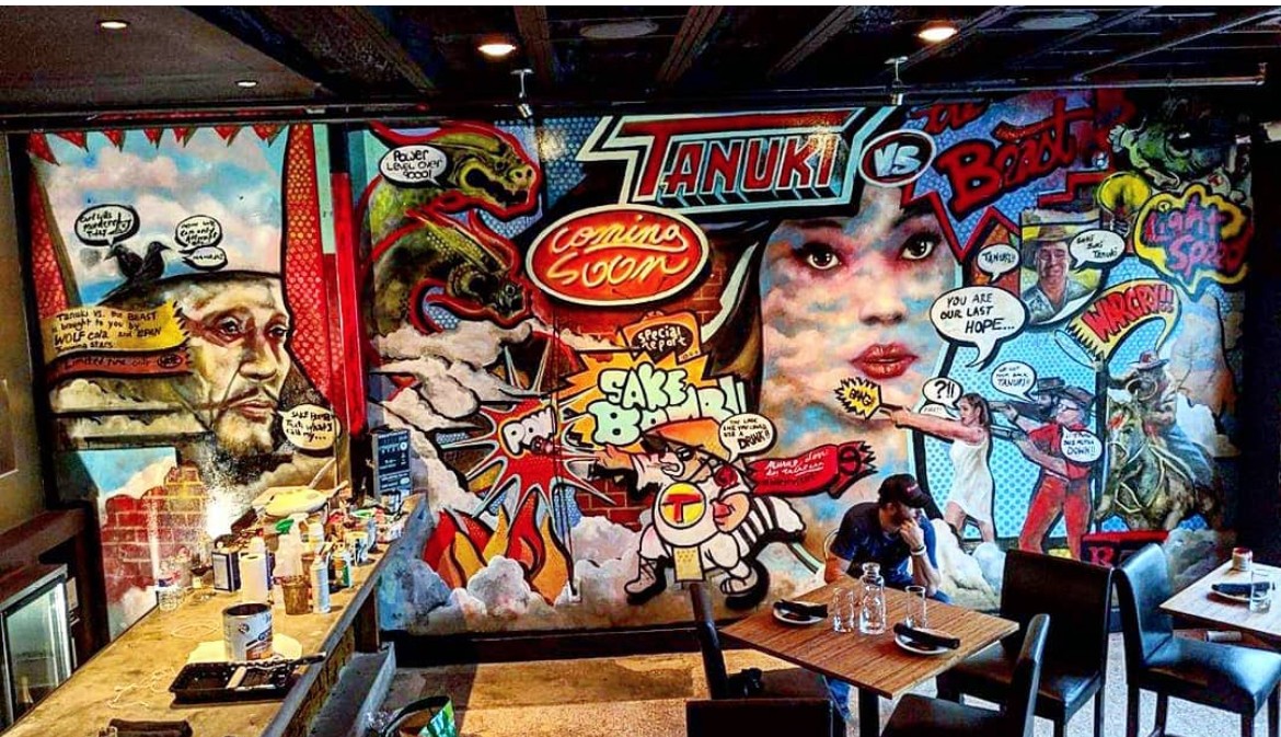 Colorful comic-book mural covers a restaurant wall behind tables, chairs, and a counter.