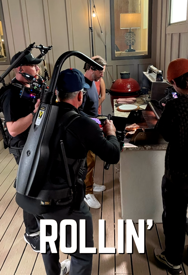 A camera crew films people gathered around a kitchen island, with “ROLLIN’” printed at the bottom.