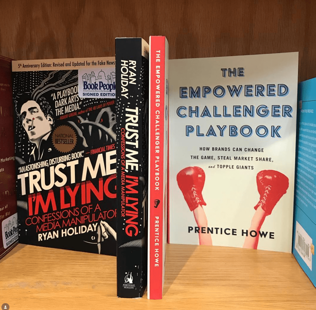 Three books stand on a wooden shelf, including titles about trust and empowered challengers.