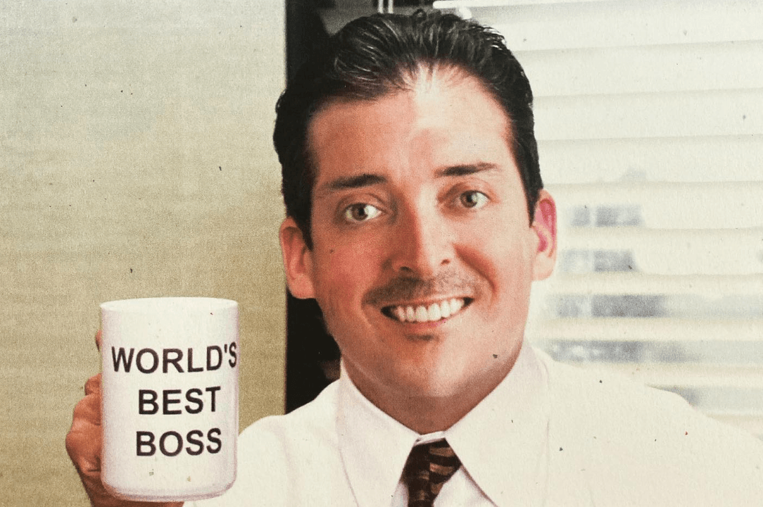 A smiling person in a tie holds a mug labeled “World’s Best Boss.”