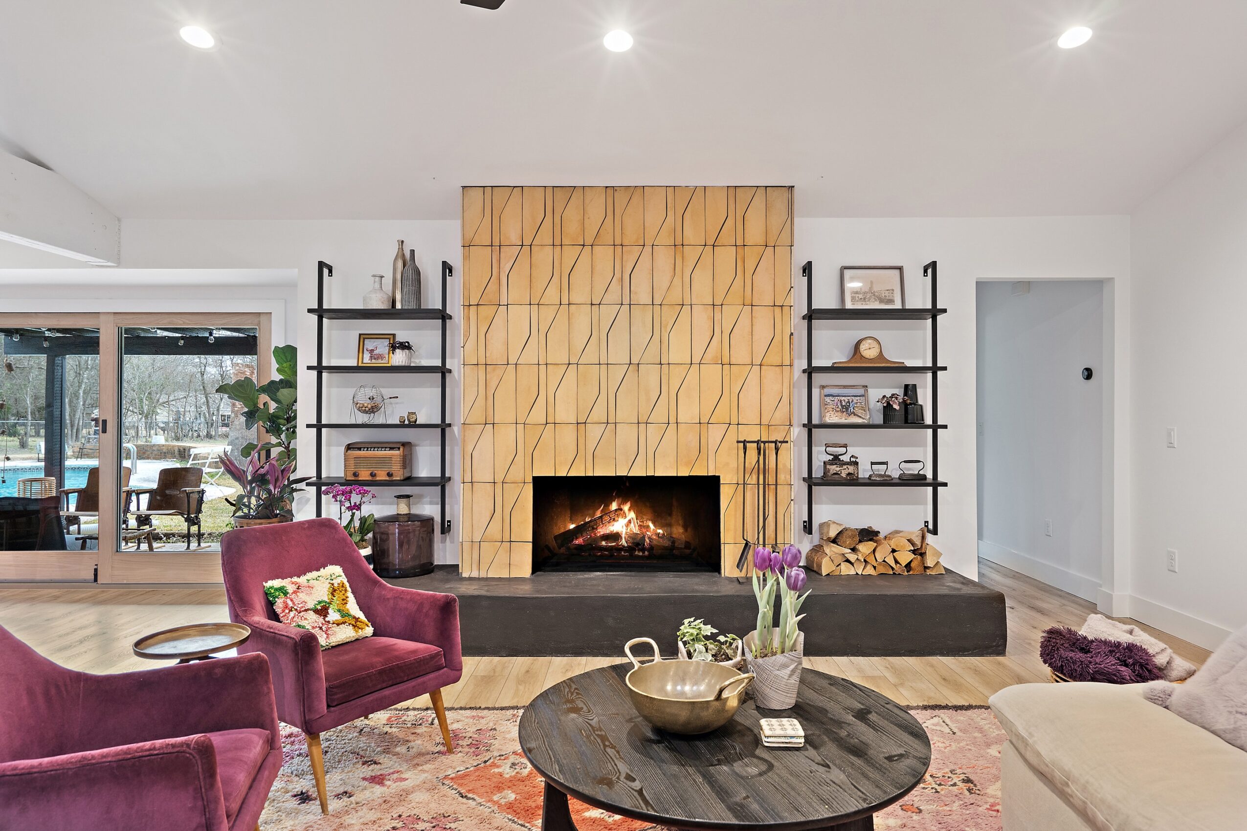 Living room with a tall wood-paneled fireplace, dark round coffee table, burgundy chairs, and a light sofa.