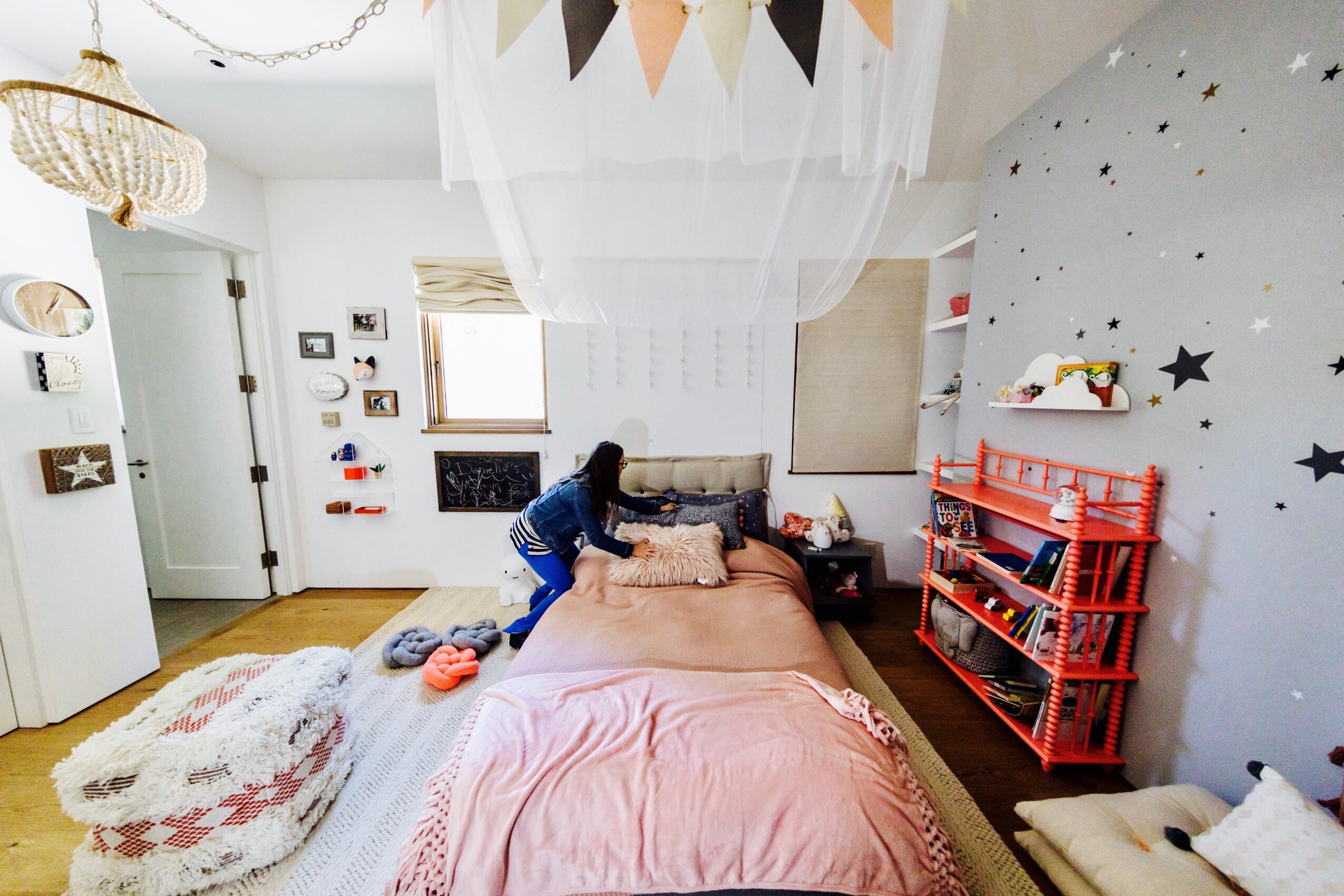 A bedroom with a pink bed, a red toy shelf, wall stars, and a hanging canopy.